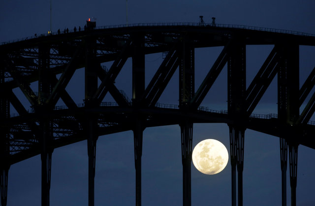Participants in a Sydney Harbour Bridge Climb (L) walk across the western span of the famous Australian landmark as the Super Moon rises after sunset, November 14, 2016. (Photo: Reuters)