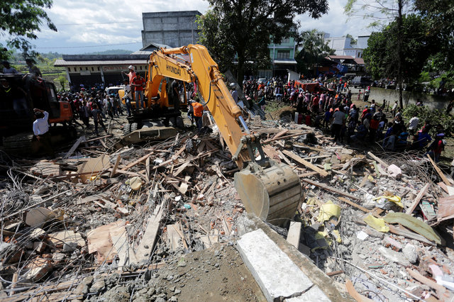 Rescue workers use heavy equipment to search for victims in a collapsed building. (Photo: Antara Foto/ Irwansyah Putra/ via Reuters)